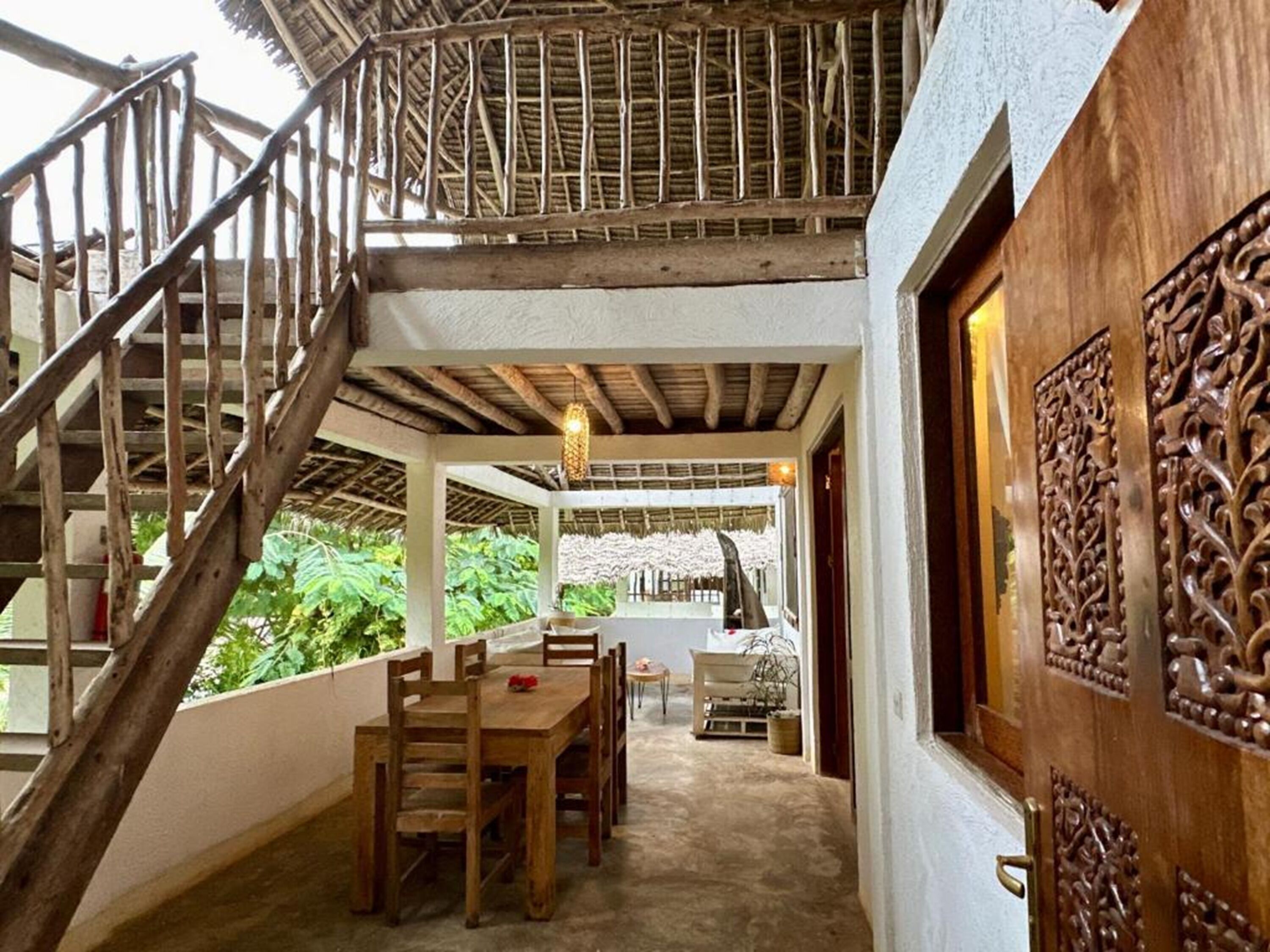 A wooden staircase leading to an upper level, a dining area with a table and chairs, and a decorative wooden door.