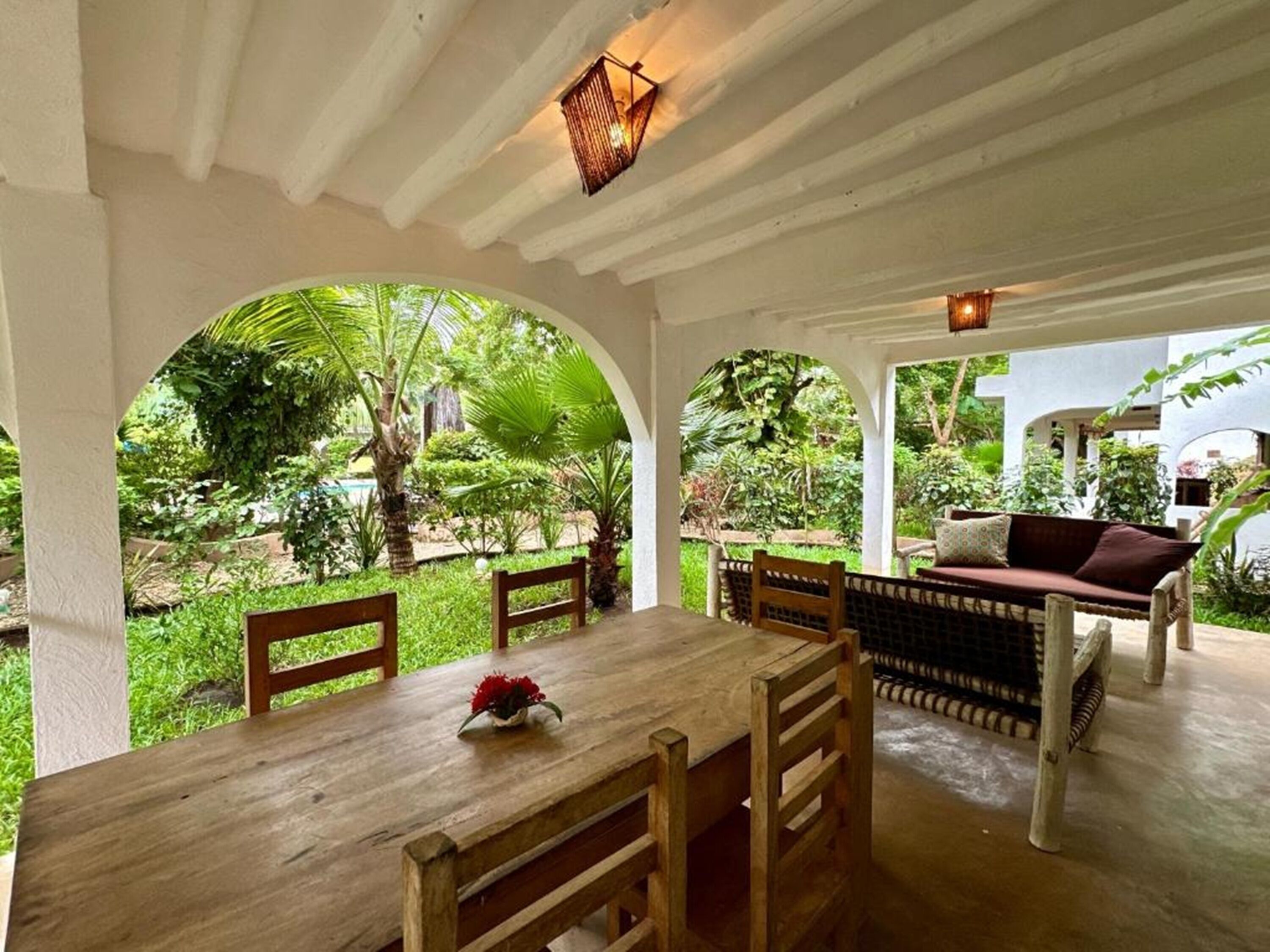 An outdoor patio with a wooden table and chairs, a cushioned bench, and a hanging light fixture.