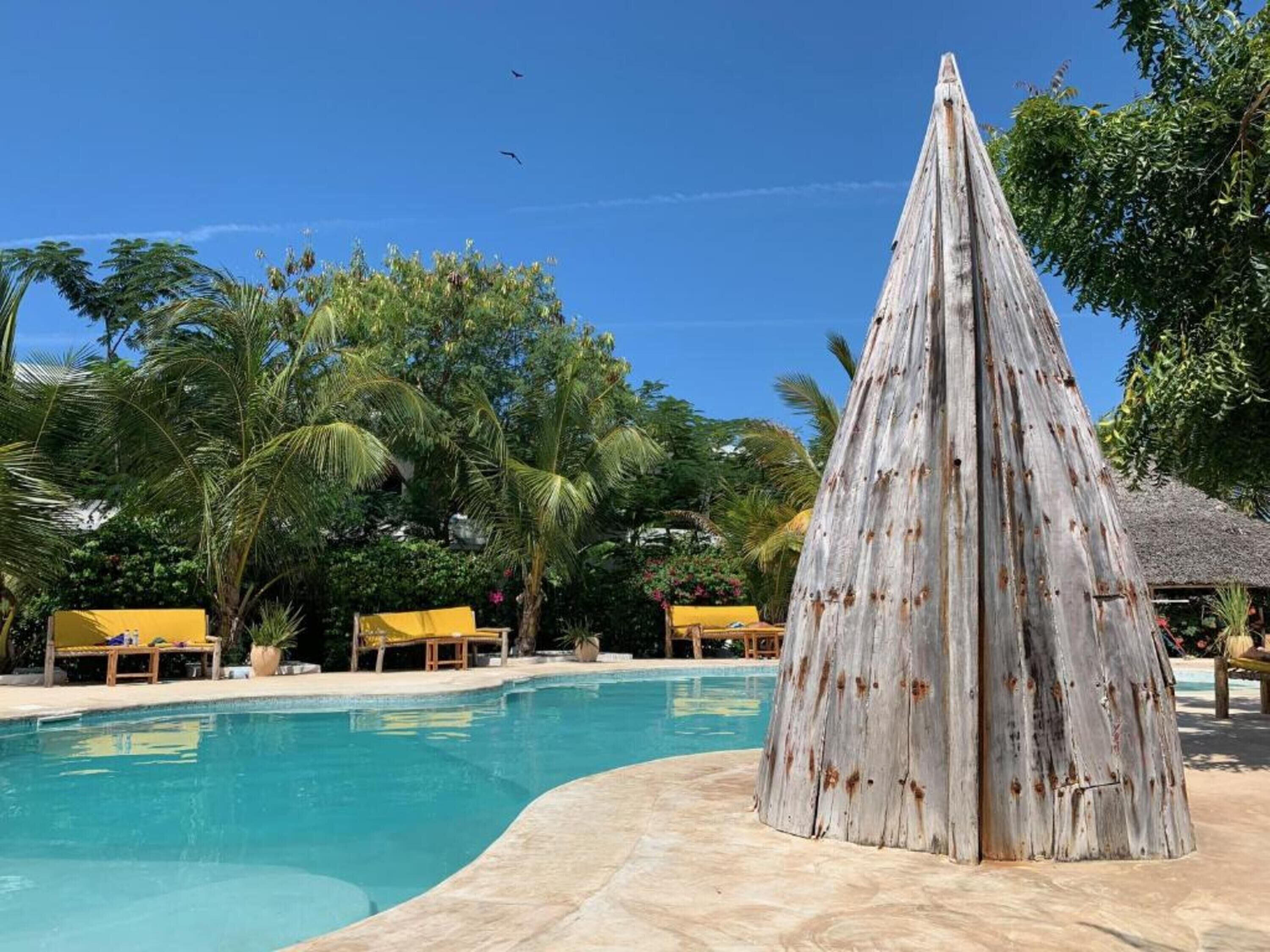 A pool area with a wooden structure, palm trees, and lounge chairs.