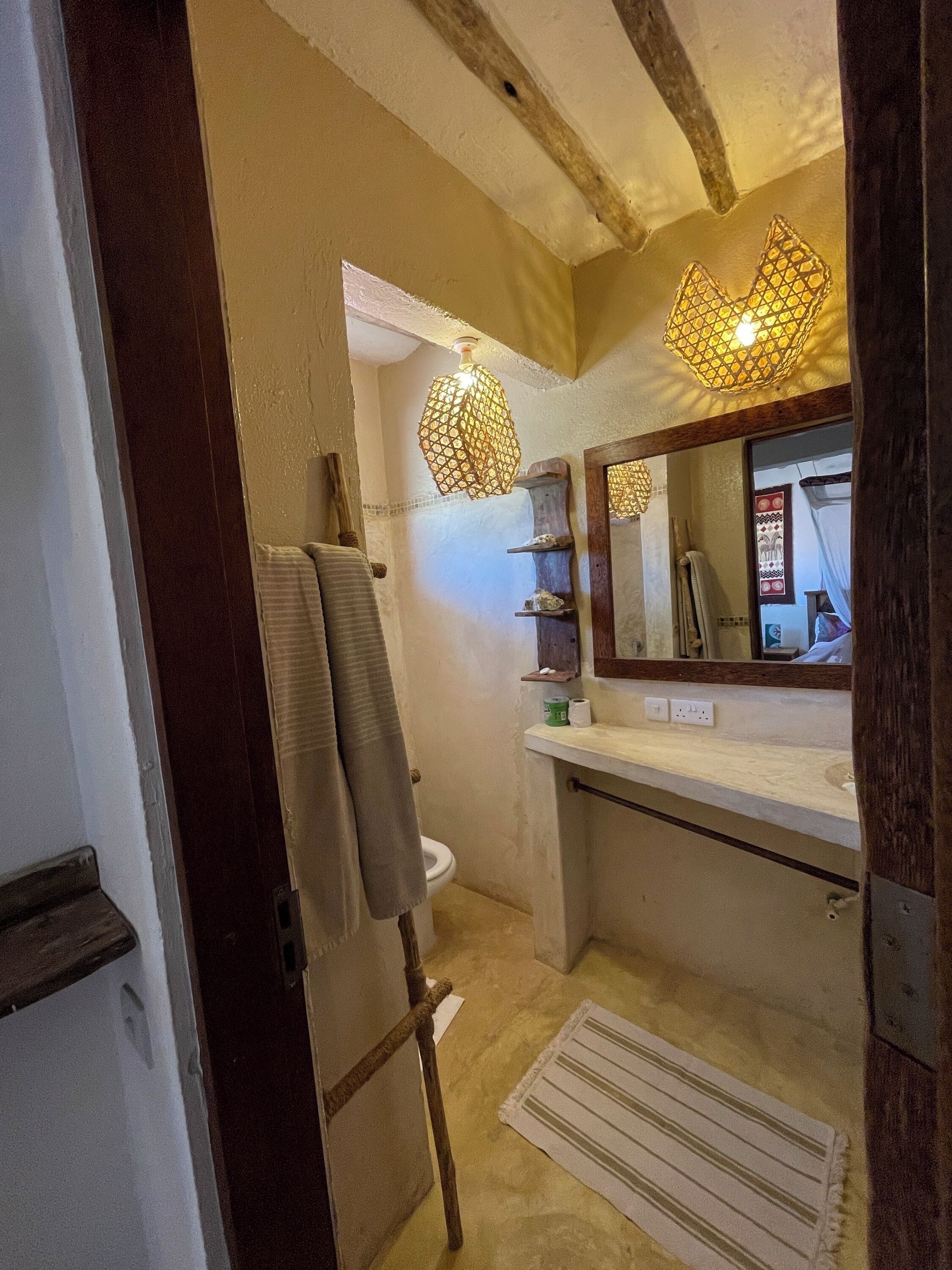 A bathroom with a wooden beam ceiling, a towel rack, a sink with a mirror, and a hanging light fixture.