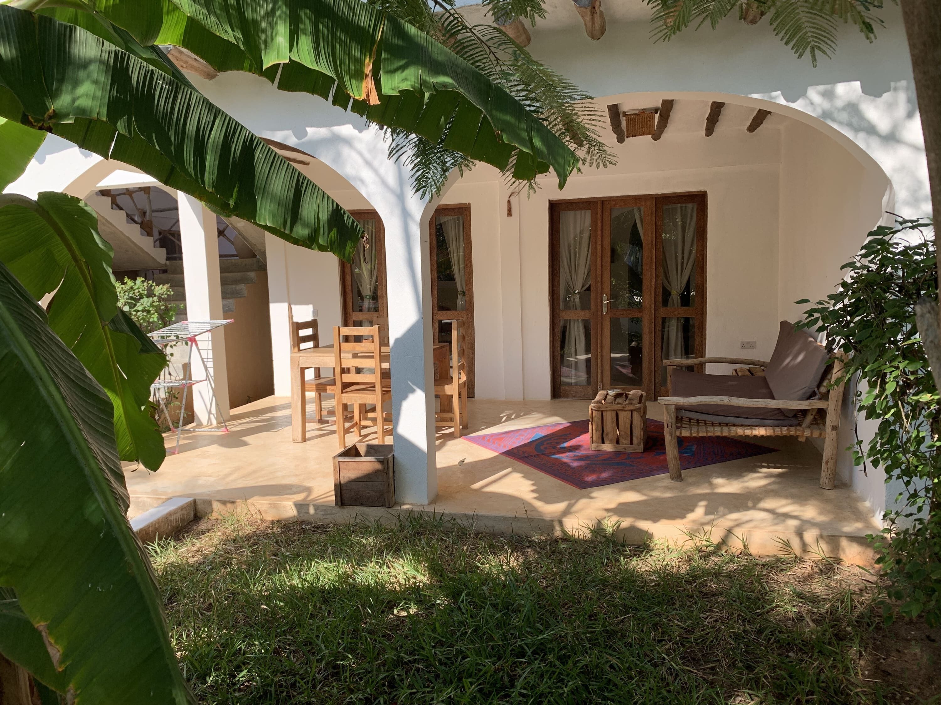 A covered outdoor seating area with wooden furniture, a patterned rug, and a view of the building's interior.