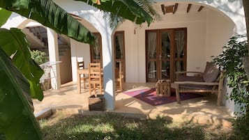A covered outdoor seating area with wooden furniture, a patterned rug, and a view of the building's interior.
