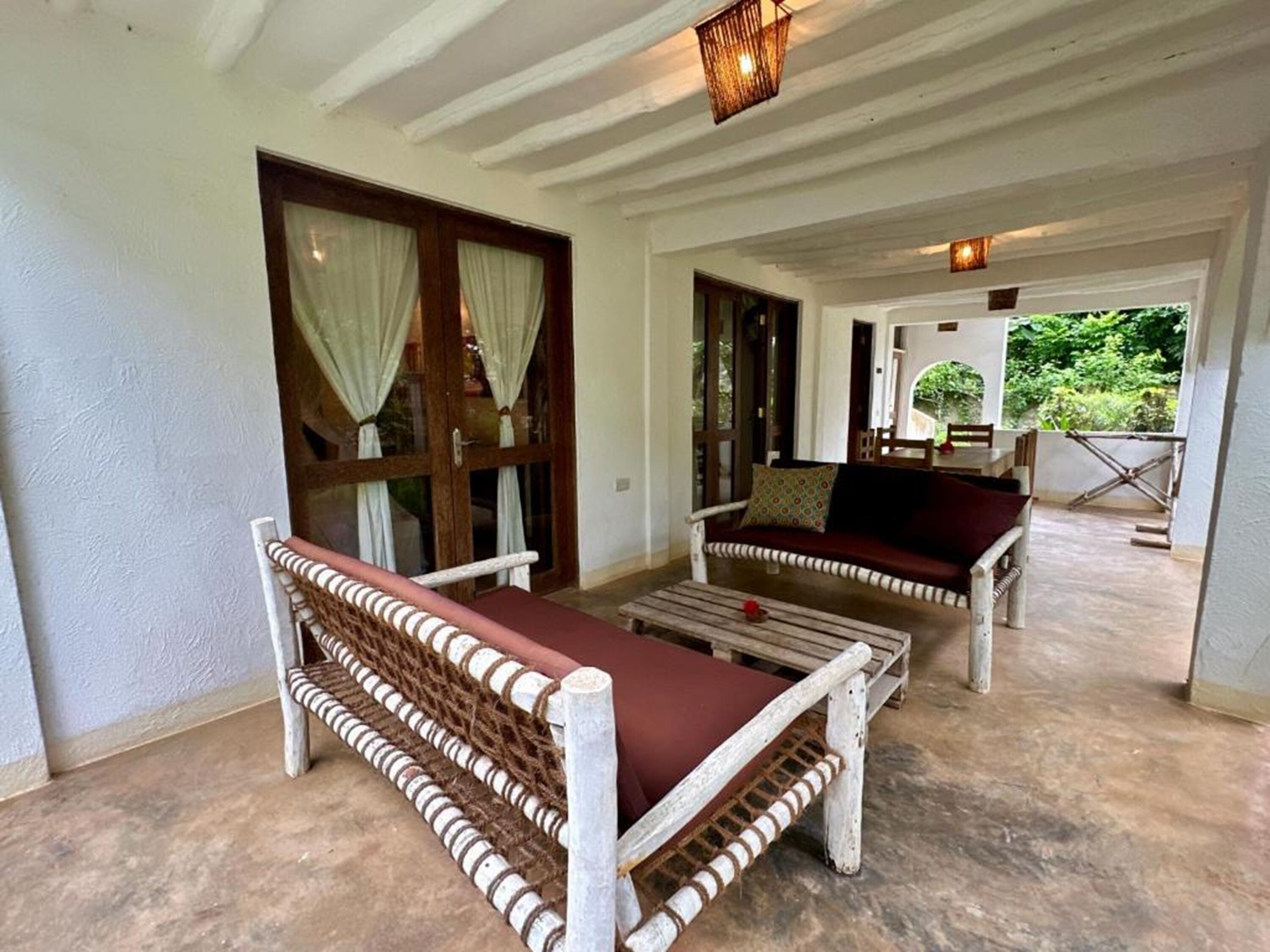 A covered outdoor seating area with wooden furniture and a view of the garden.