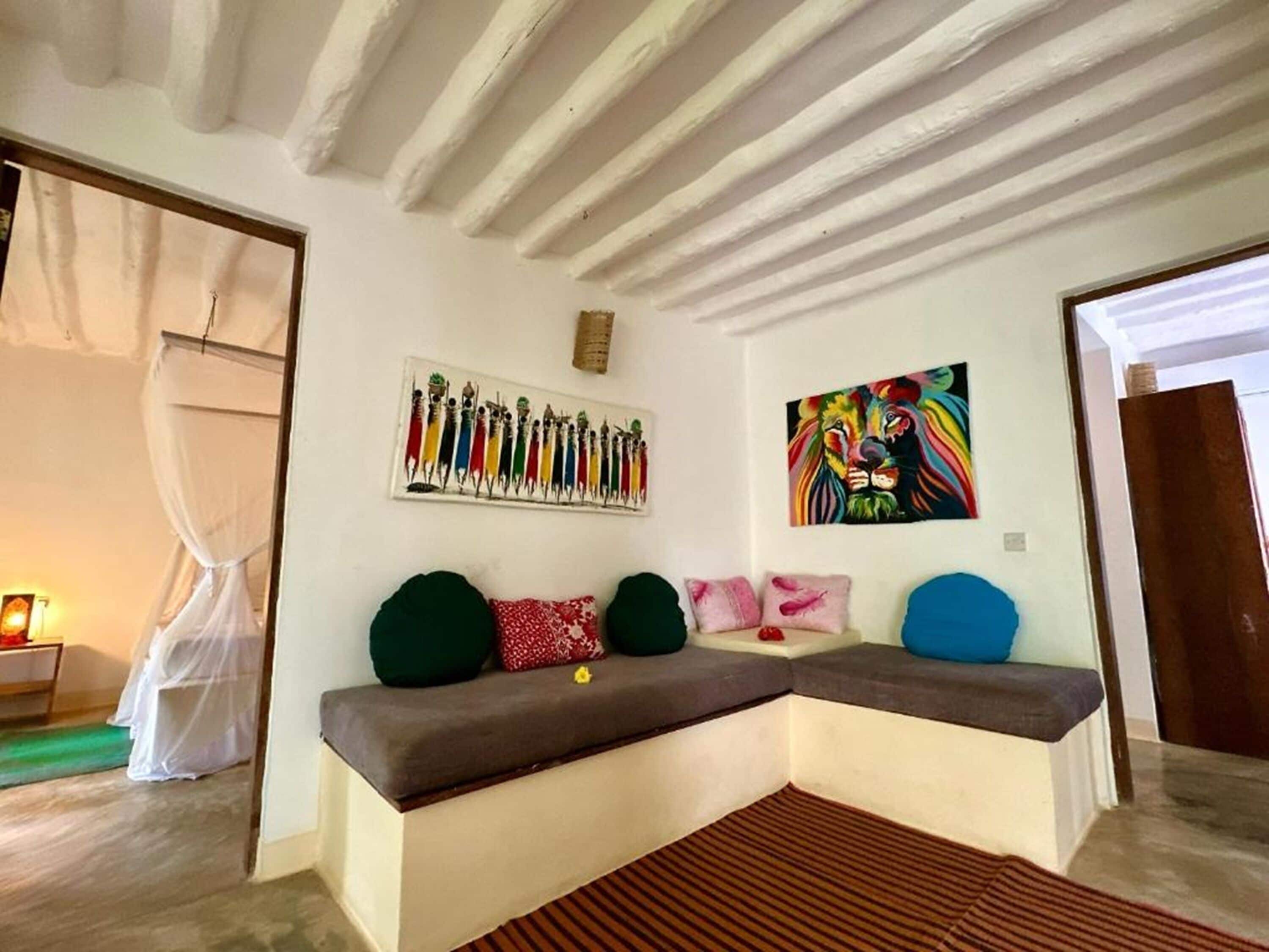 A room with a built-in bench, a painting of a lion, and a wall-mounted artwork of a colorful figure.