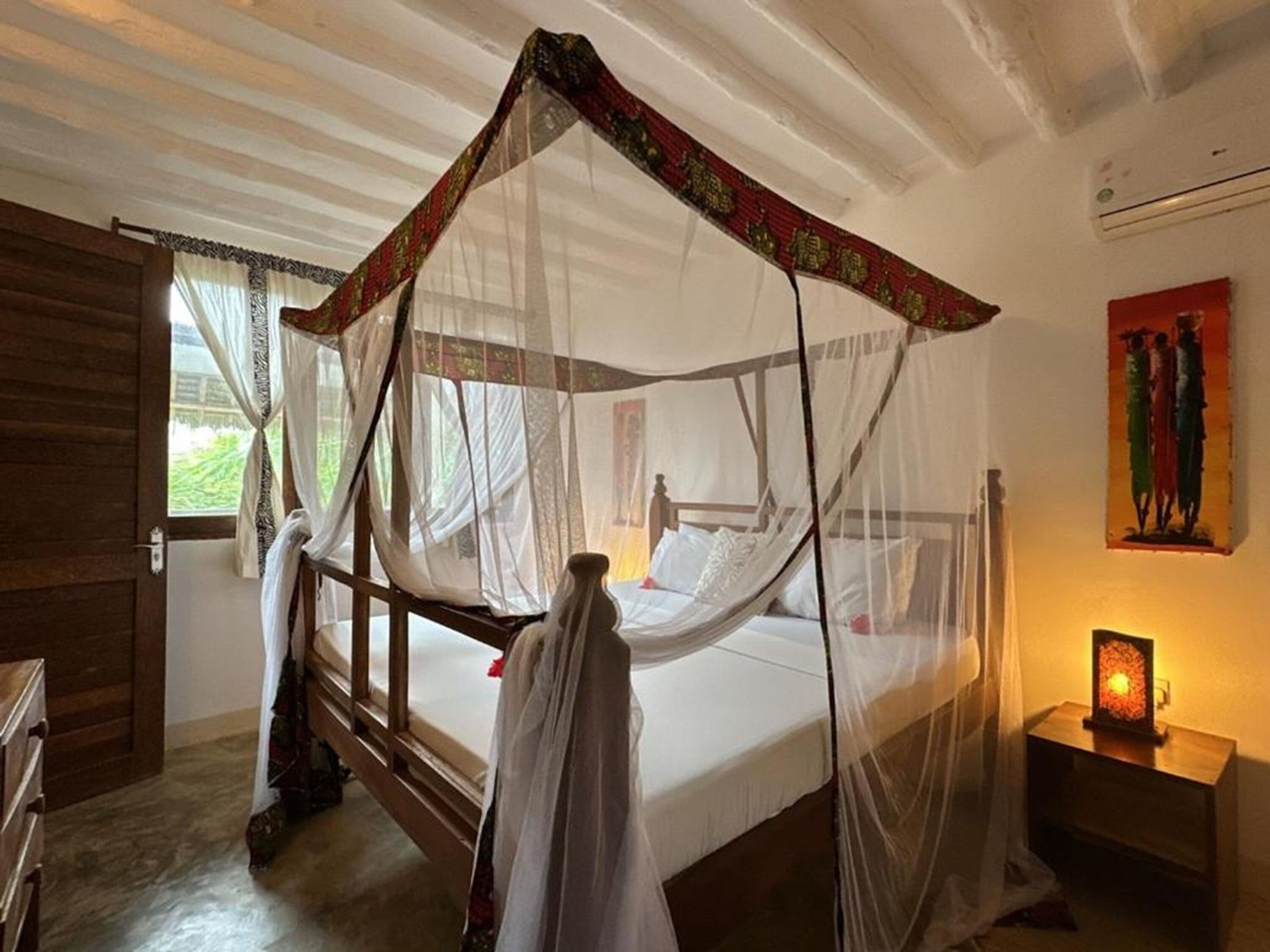 Une chambre avec un lit à baldaquin, une armoire en bois, une table de chevet avec une lampe et un tableau au mur.