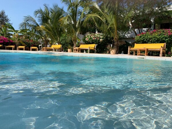 A clear pool with yellow loungers and palm trees.