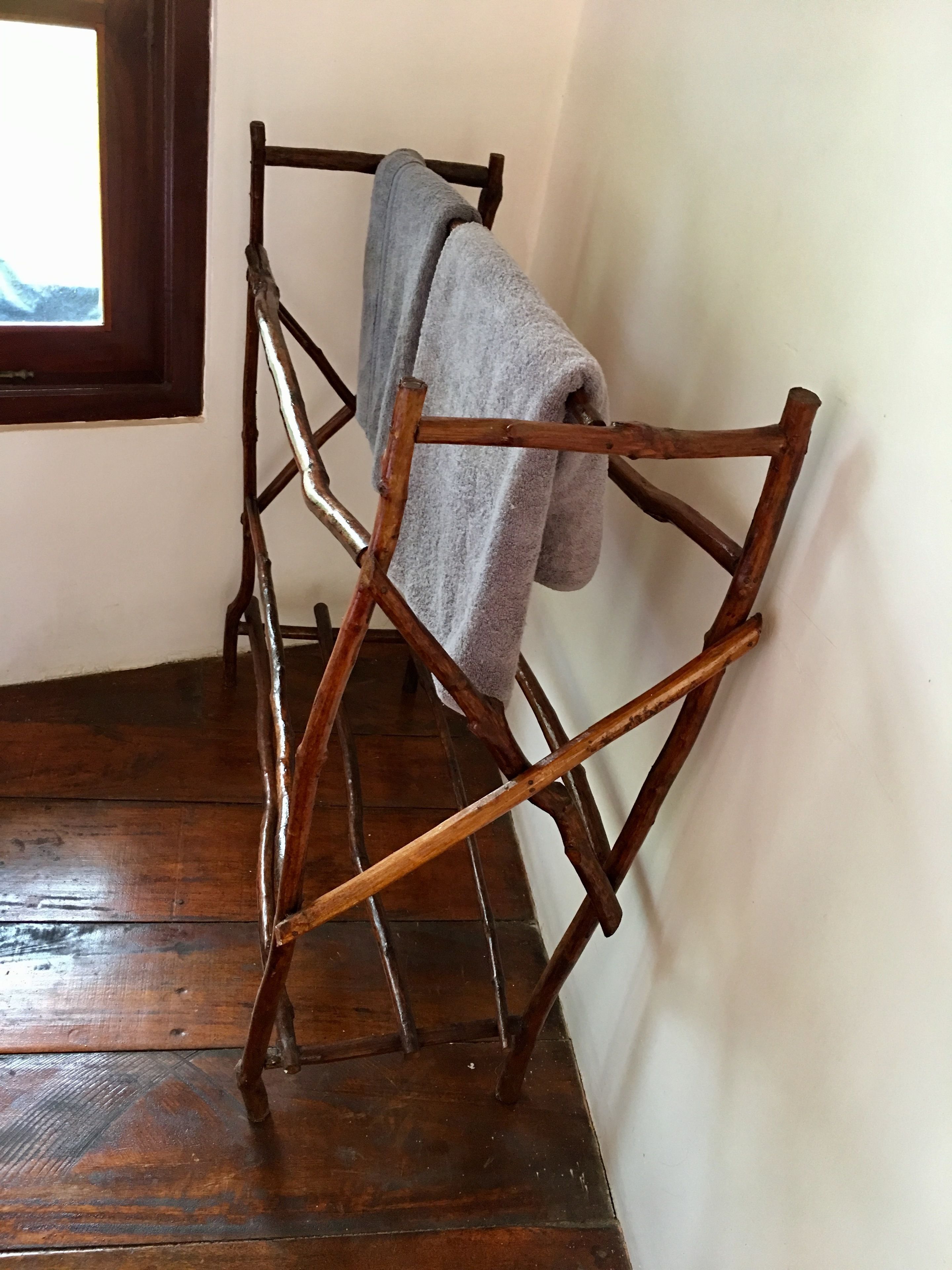 A wooden drying rack with a towel hanging on it, placed against a wall in a room with wooden flooring.