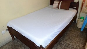 Una cama individual con sábana blanca y almohada a rayas en una habitación con pared lisa y cabecero de madera.