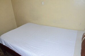 Une chambre avec un lit simple, recouverte d’une courtepointe blanche unie et dotée d’une tête de lit en bois.
