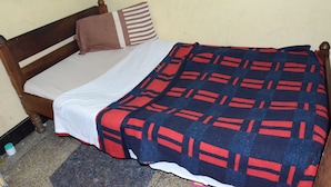 Una cama individual con cabecera de madera, colchón blanco y manta estampada en azul y rojo.