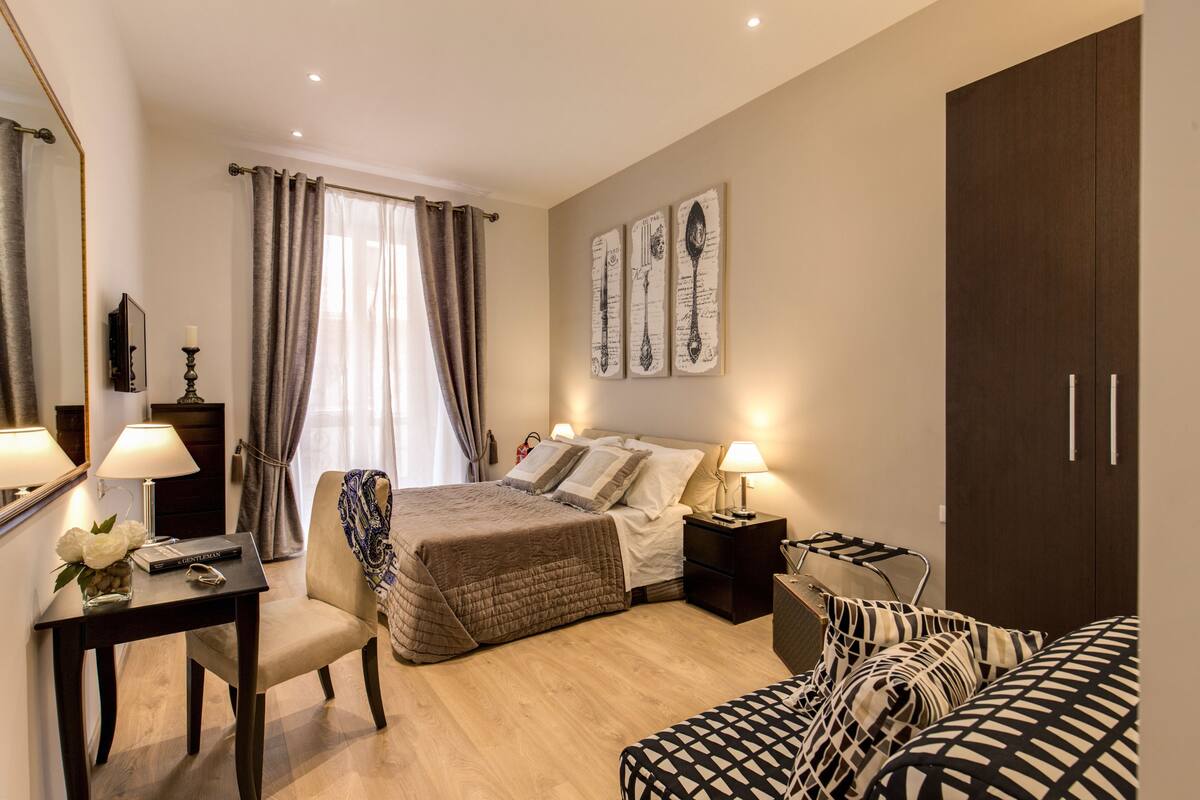 A hotel room with a bed, bedside tables, a desk, a chair, and a wardrobe.