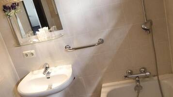 A bathroom with a white sink, a mirror, a glass shelf with toiletries, a grab bar, and a bathtub.