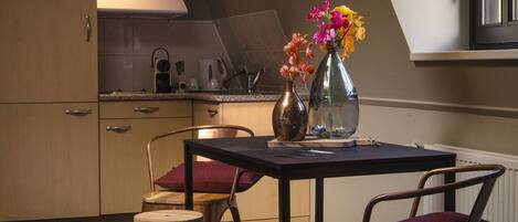 Cocina compacta con armarios de madera, encimera negra y una mesa de comedor con dos taburetes. Hay dos jarrones con flores sobre la mesa.