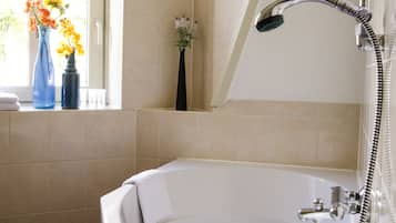 A bathroom with a bathtub, a shower, and two vases with flowers on a windowsill.