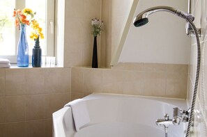 A bathroom with a bathtub, a shower, and two vases with flowers on a windowsill. - Hotel Jambon (Uden)