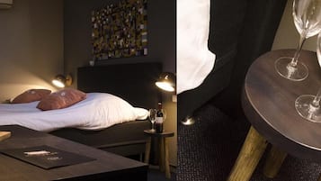 Une chambre avec un lit, une table de chevet ornée d’un vase de fleurs, une bouteille de vin et des verres.