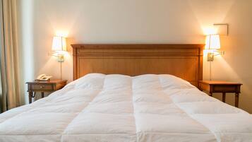 Una cama bien hecha con cabecera de madera, dos mesitas de noche con lámparas, y un teléfono sobre la mesa de la izquierda.