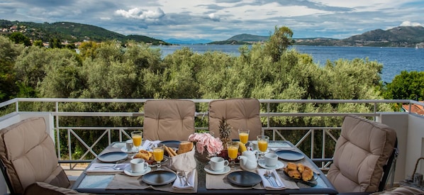 A dining table set for breakfast with a view of a lake and hills.