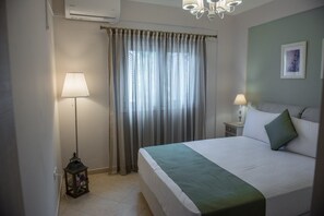 A hotel room with a bed, a nightstand with a lamp, a window with curtains, and a wall-mounted air conditioner.