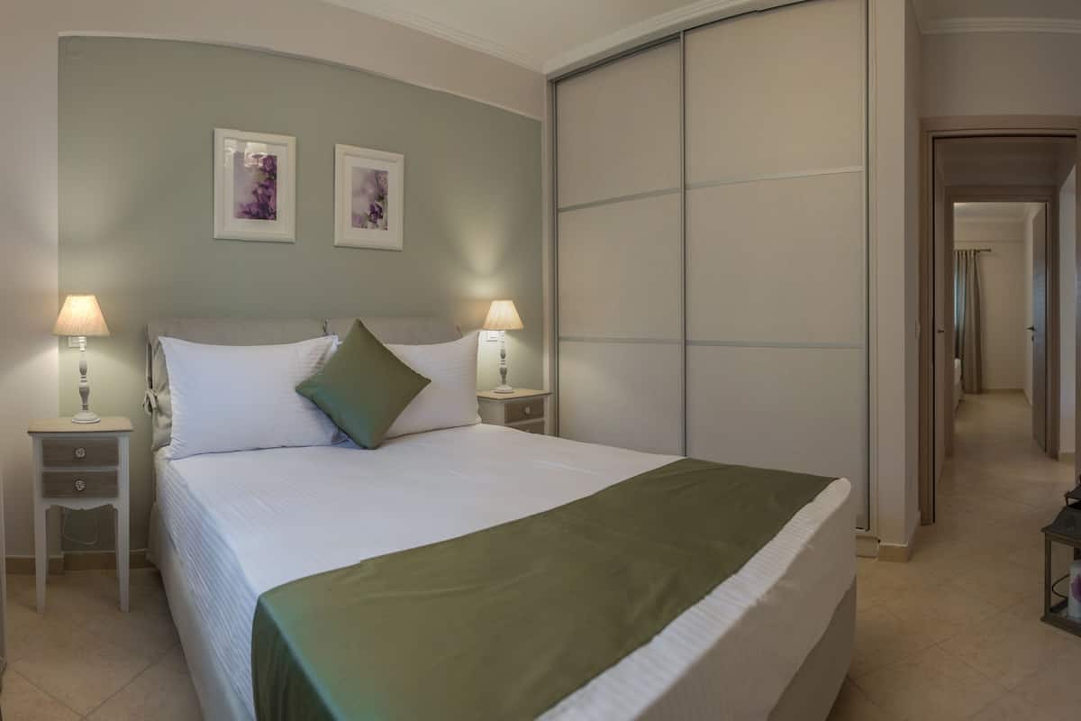 A neatly made bed with a green throw, two bedside lamps, and two framed pictures on the wall.