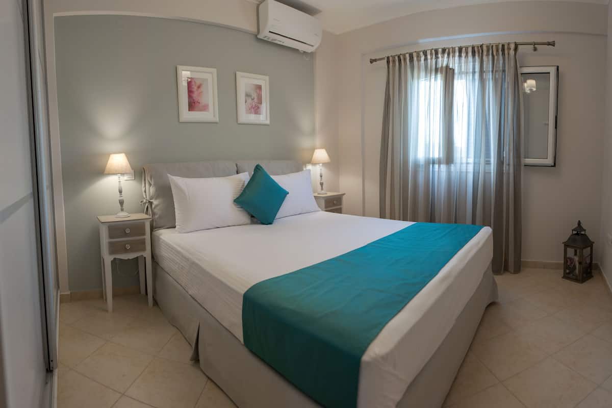 A neatly made bed with a teal bedspread, two bedside lamps, and a small nightstand with a lamp.