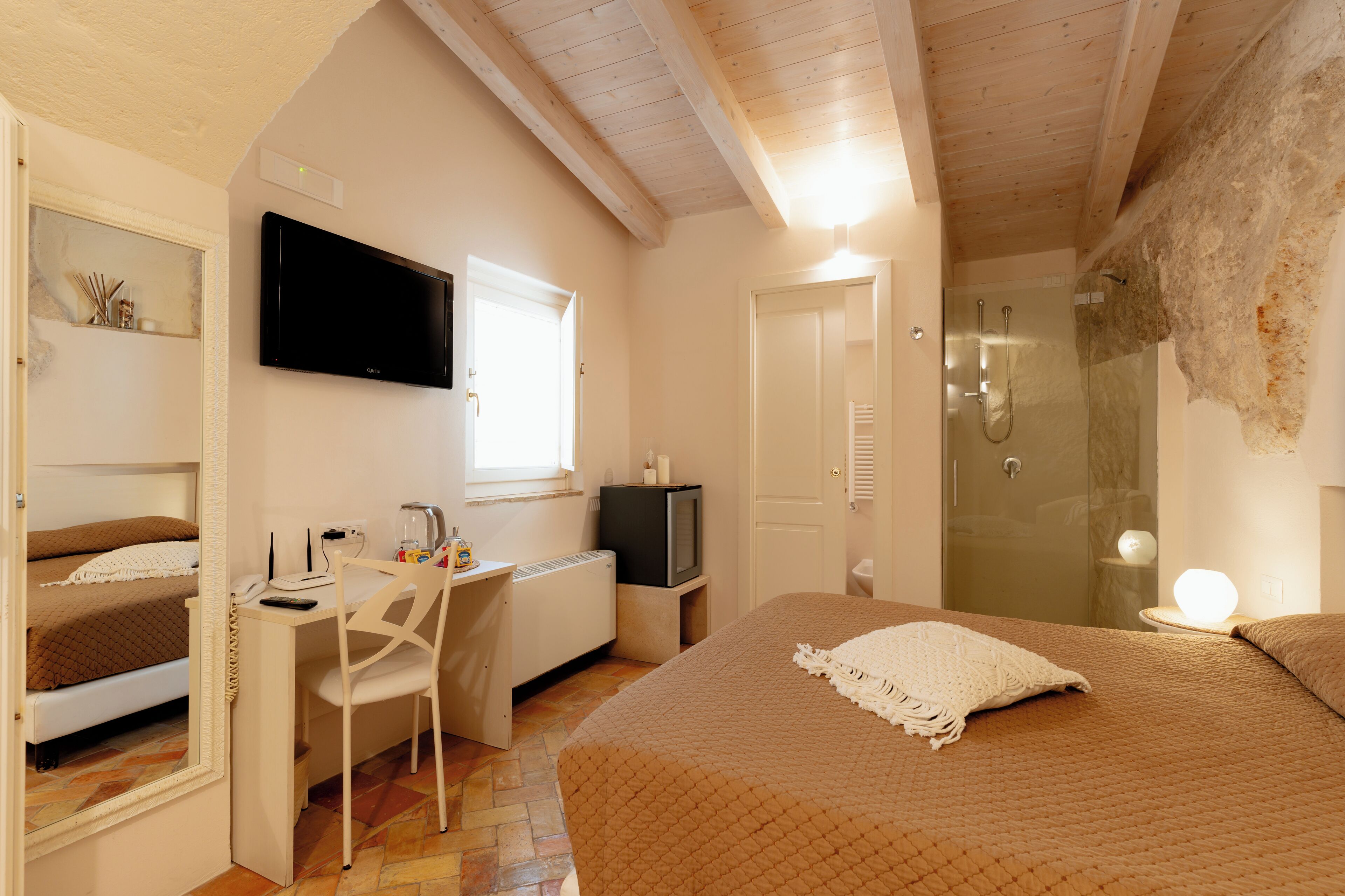 A bedroom with a bed, a desk with a chair, a television, and a shower.