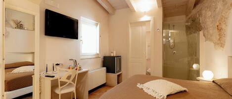 A bedroom with a bed, a desk with a chair, a television, and a shower.