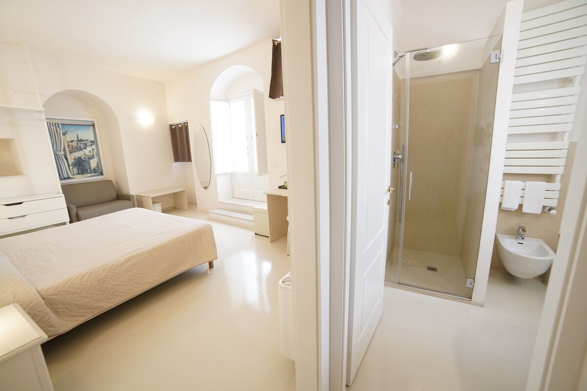 A modern bedroom with a bed, a bathroom with a shower, and a hallway with a painting.