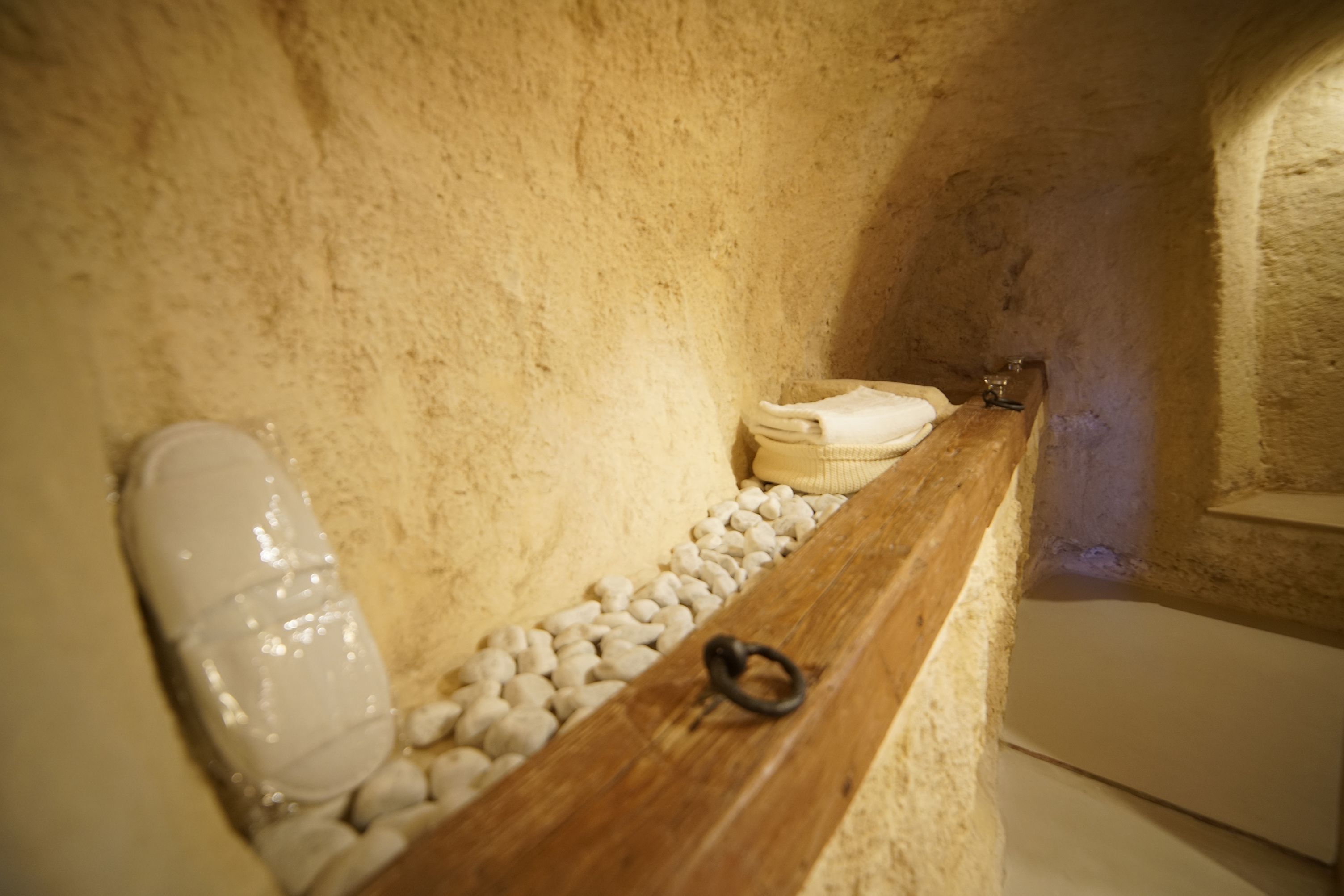 A stone-walled bathroom with a wooden bench, a white towel, and a ring on the bench.