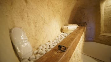 A stone-walled bathroom with a wooden bench, a white towel, and a ring on the bench.
