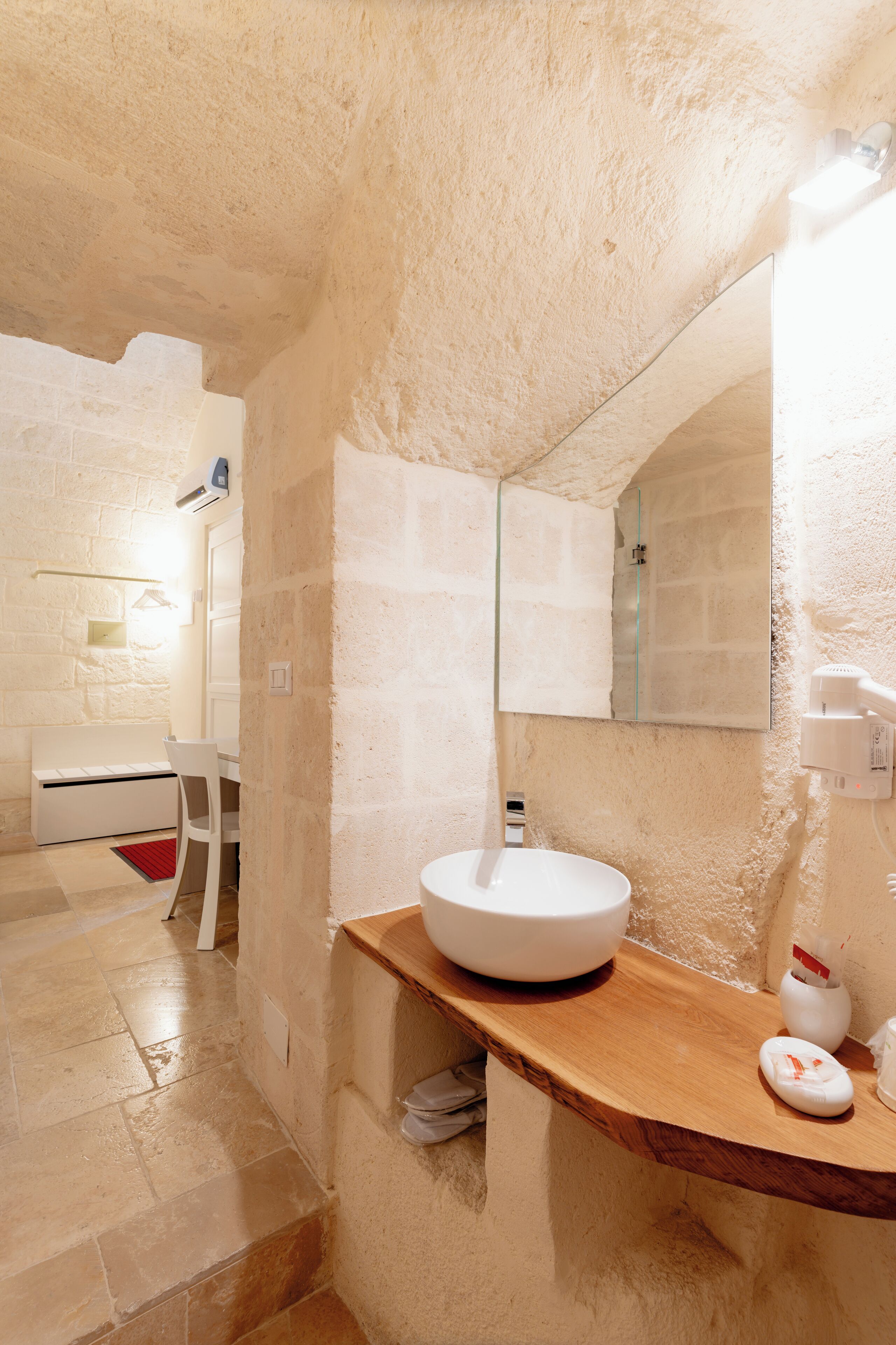 A bathroom with a white sink, a wooden countertop, a mirror, and a red rug on the floor.