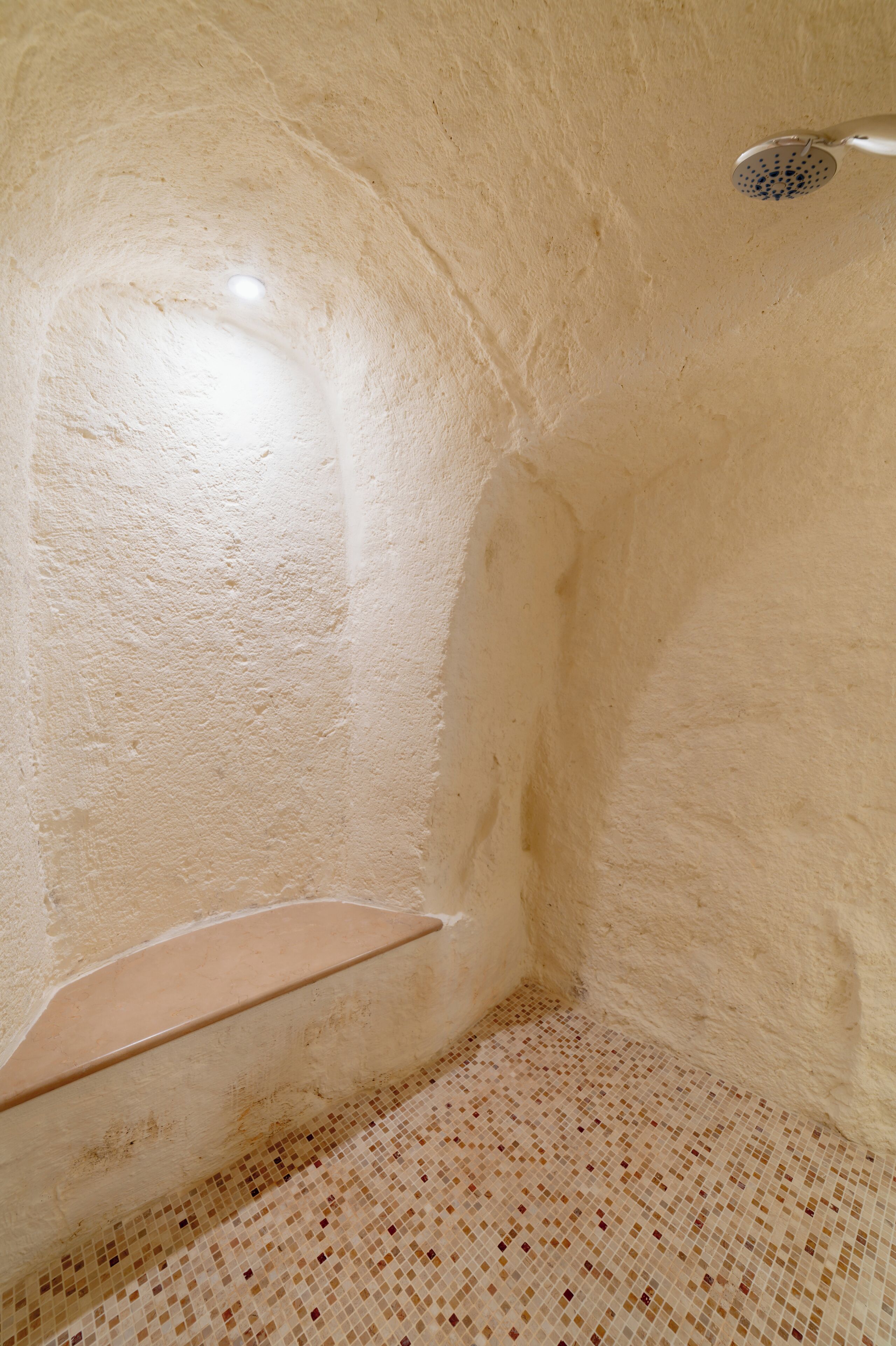 A small, enclosed space with a showerhead, a tiled floor, and a wall-mounted shelf.