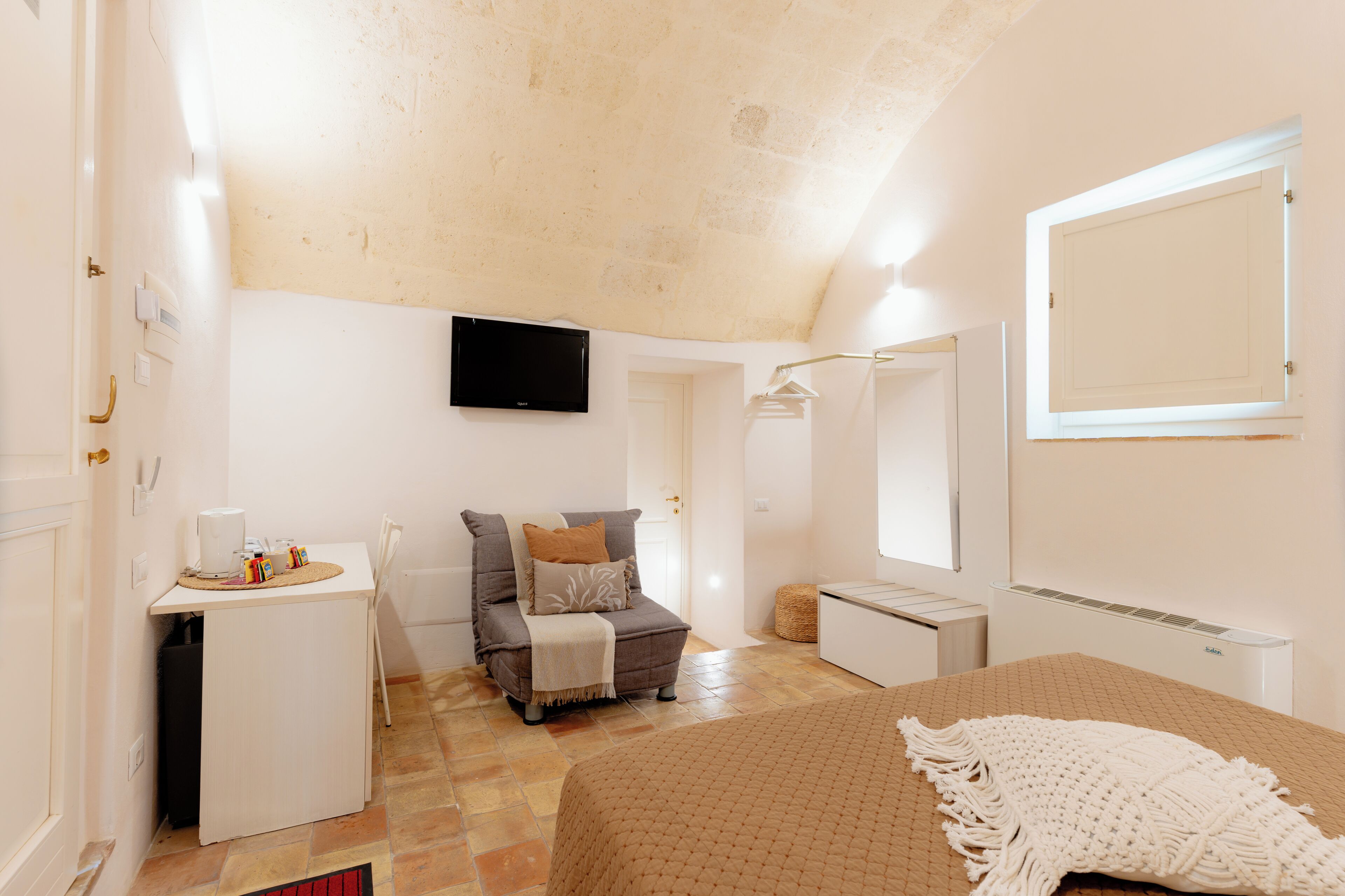 A bedroom with a bed, a desk, a chair, a sofa, a television, and a window.