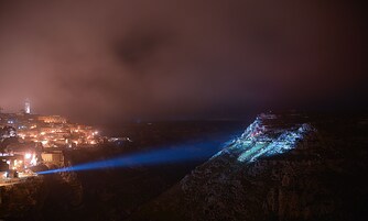 Una vista nocturna de un pueblo histórico con edificios iluminados y un acantilado destacado.