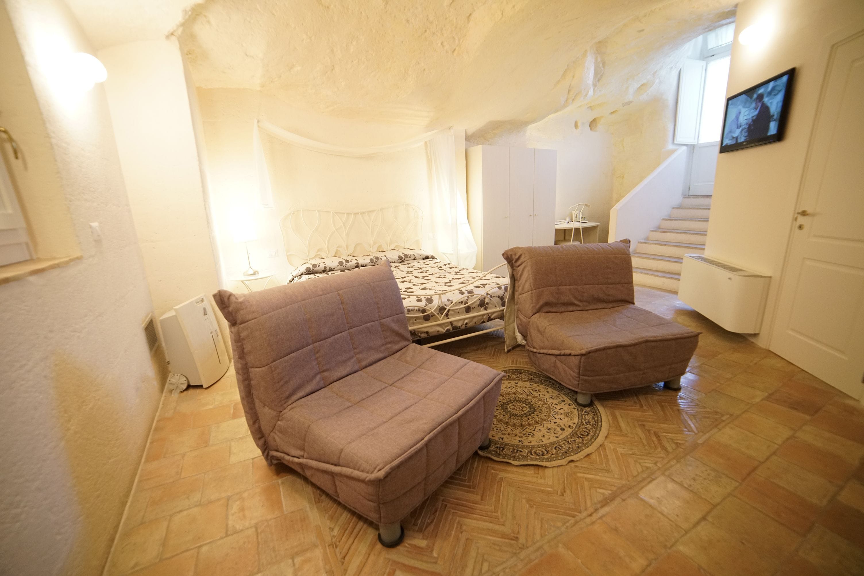 A bedroom with a bed, two armchairs, a small table, and a television.