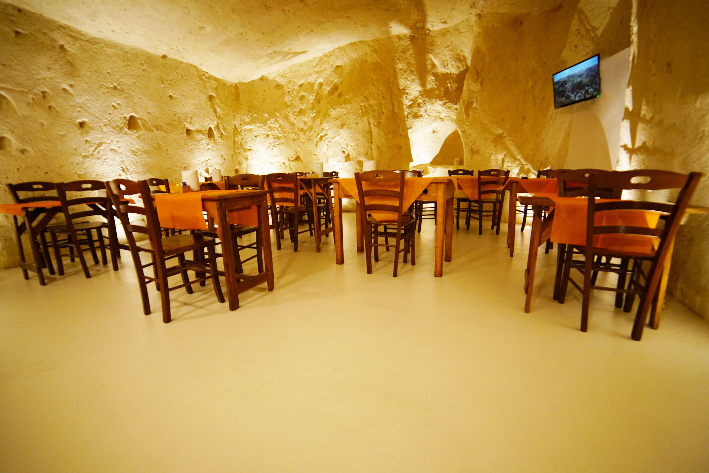 A dining area with wooden tables and chairs, a flat-screen TV mounted on the wall, and a cave-like interior.