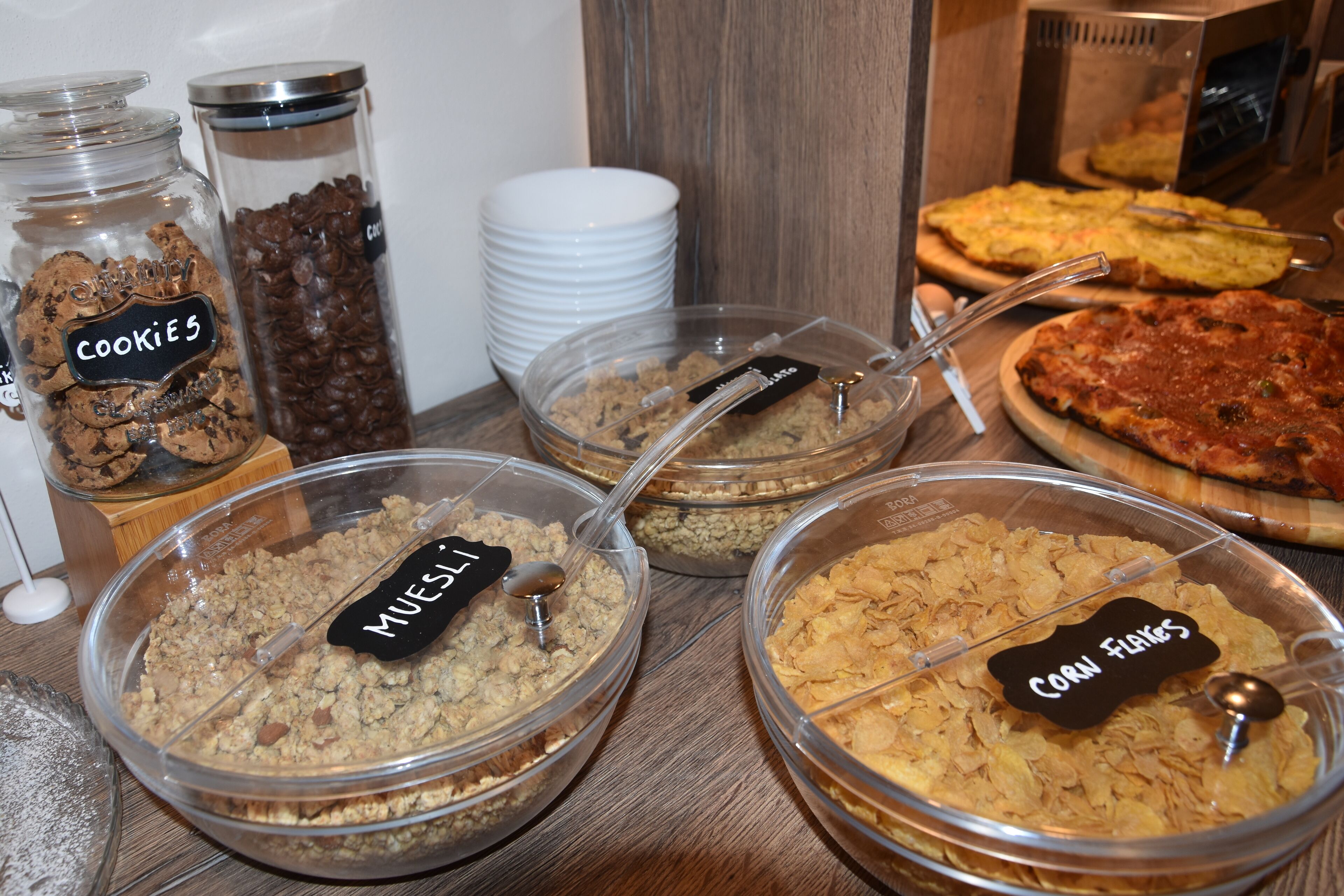 Un bufé con recipientes etiquetados de galletas, muesli y copos de maíz.