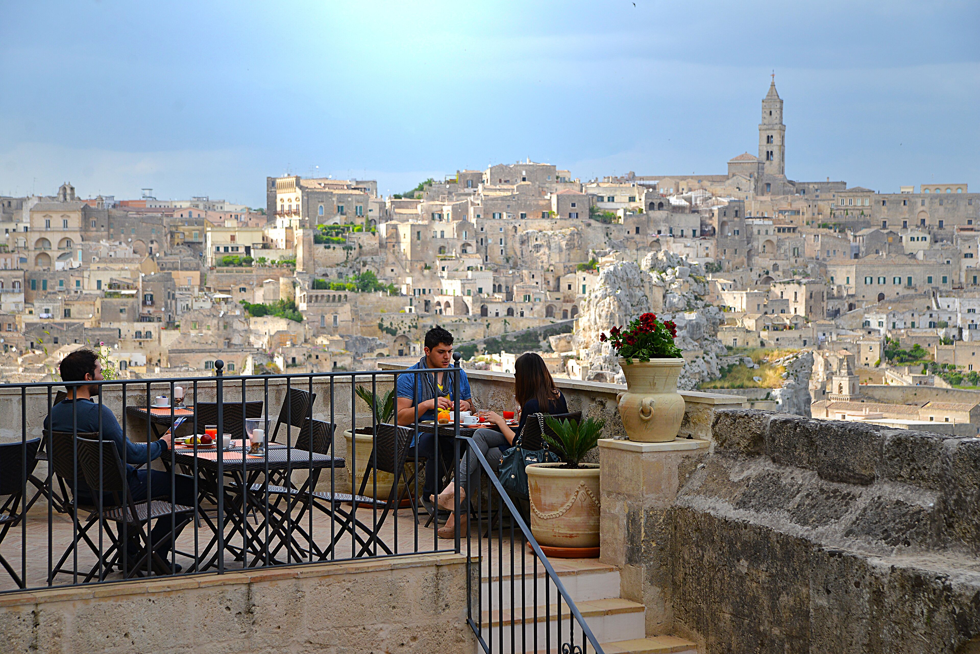 A terrace with a view of a historic cityscape, featuring stone buildings and a prominent tower.
