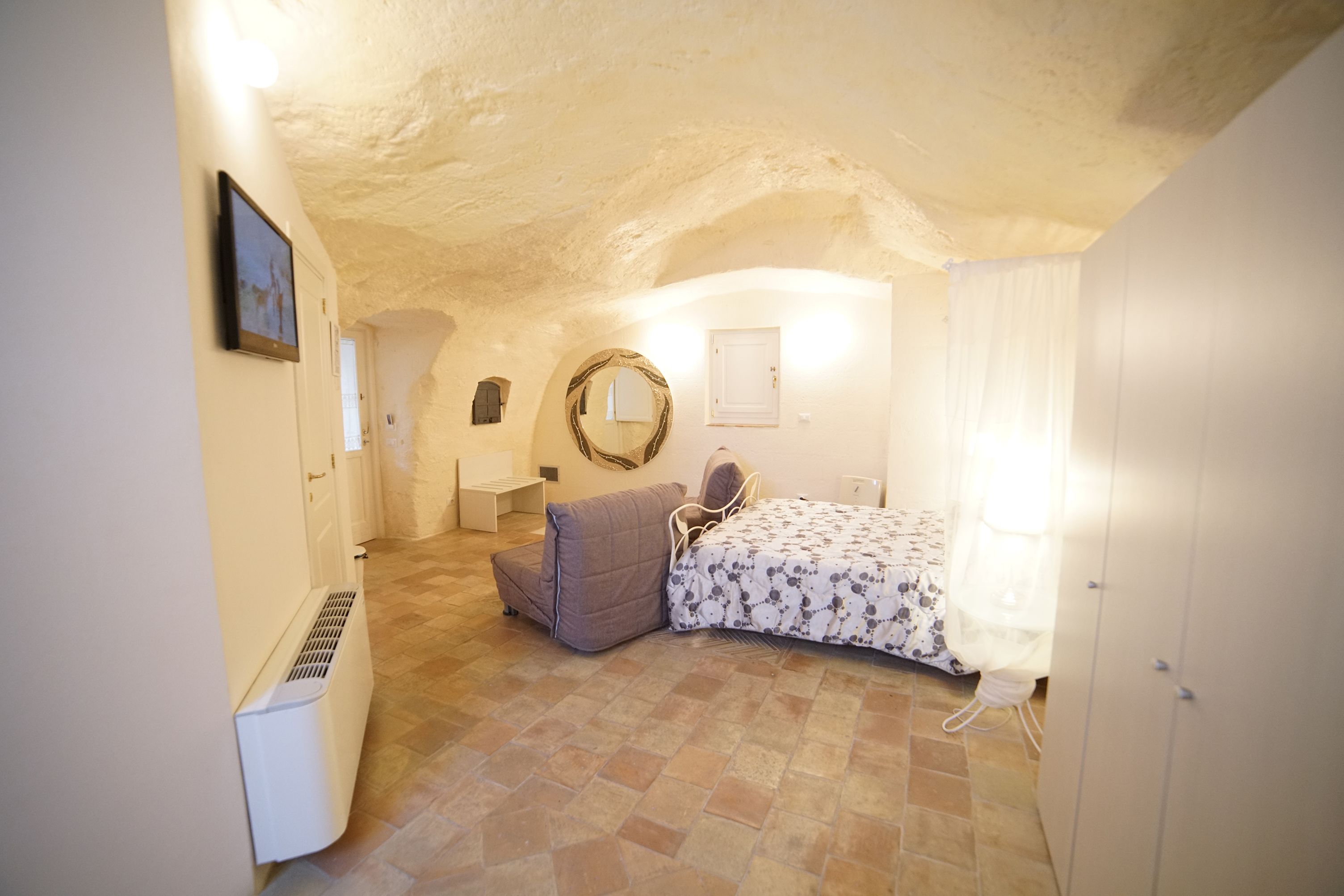 A bedroom with a bed, a bedside table, a chair, a wardrobe, and a mirror on the wall.
