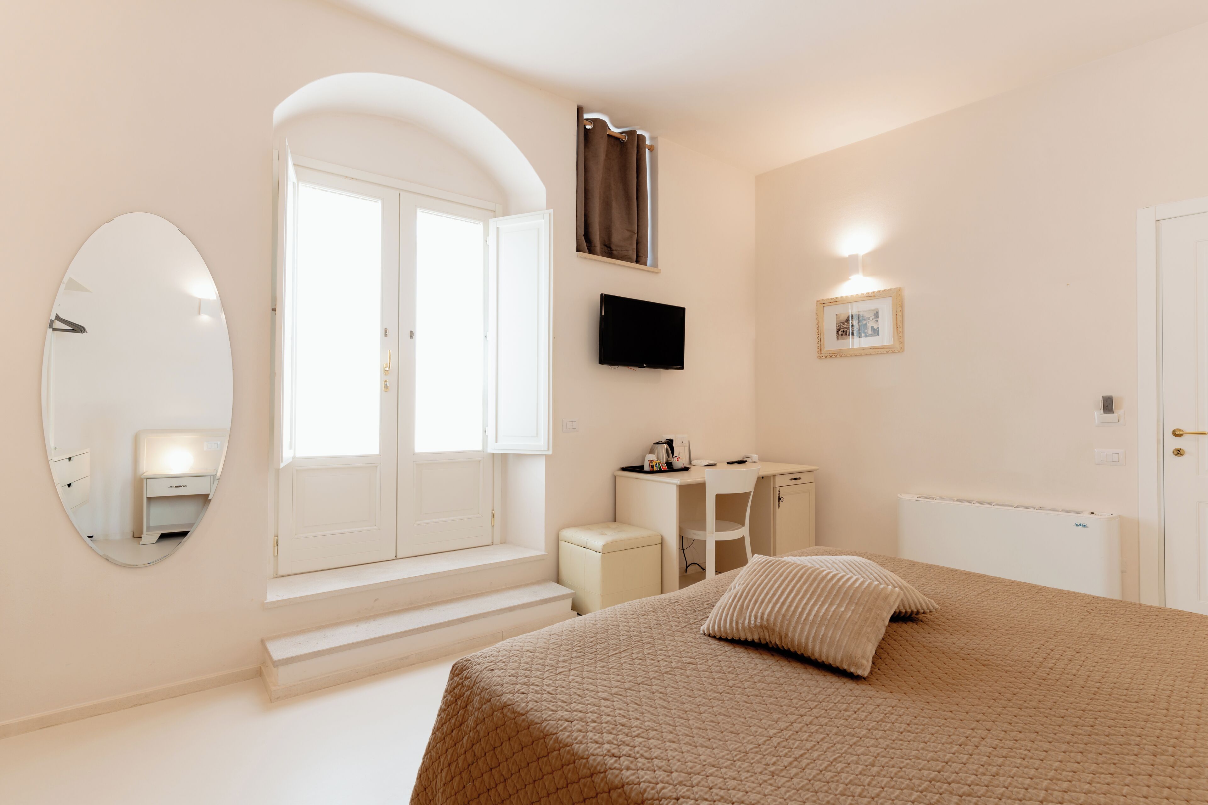 A bedroom with a bed, a desk, a chair, a television, a mirror, and a window.