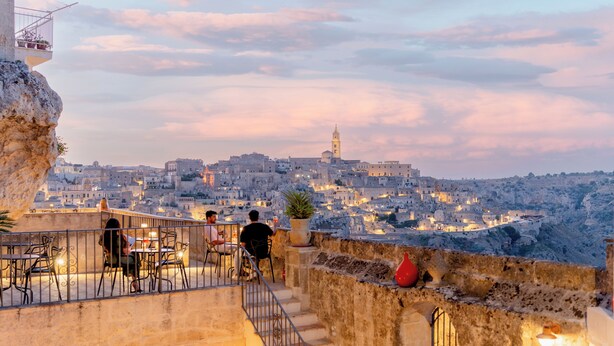 A terrace with outdoor seating overlooking a cityscape at dusk. - Il Belvedere (Matera)