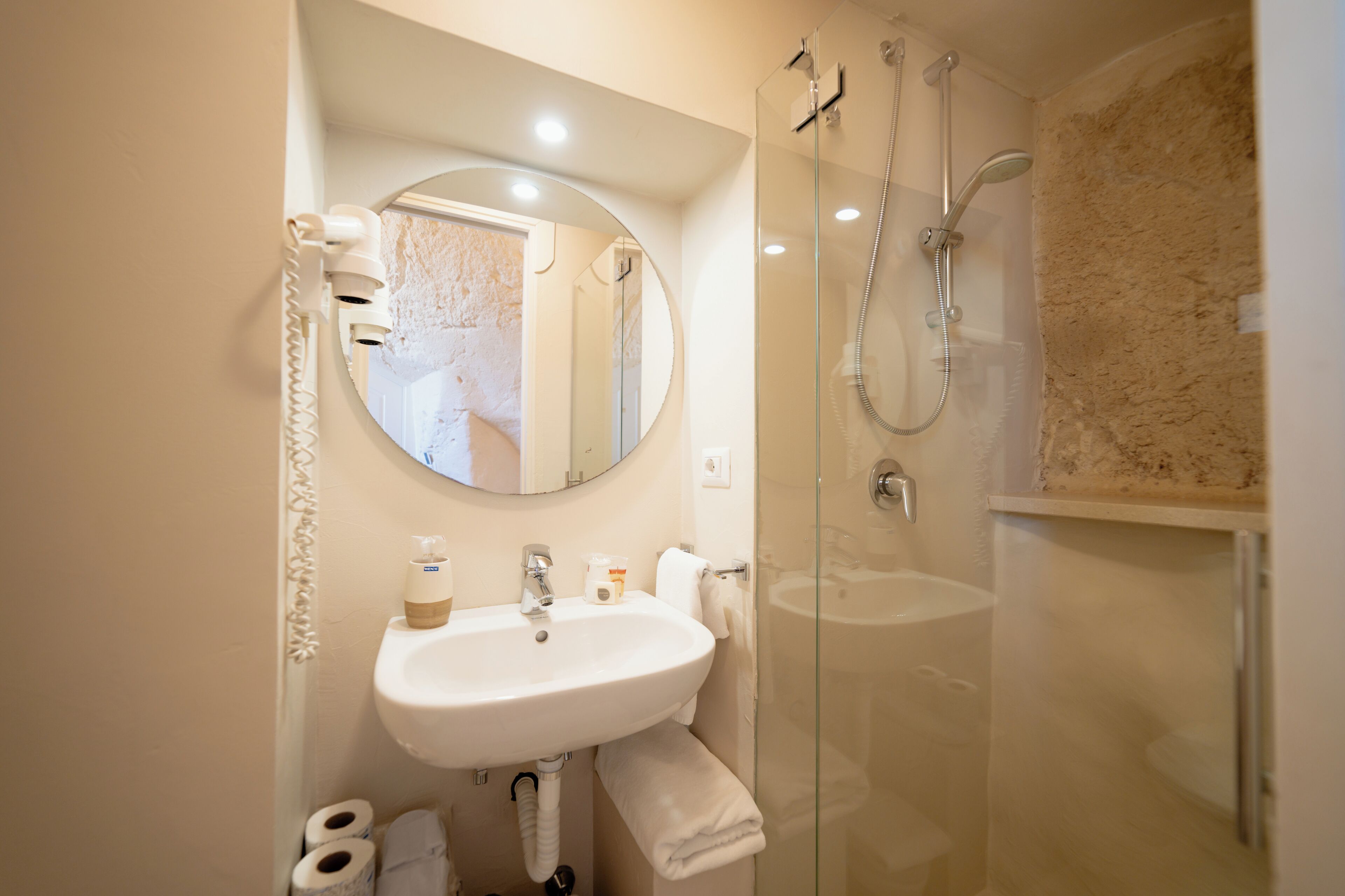 Een moderne badkamer met een douchecabine van glas, een ronde spiegel en een witte wasbak.