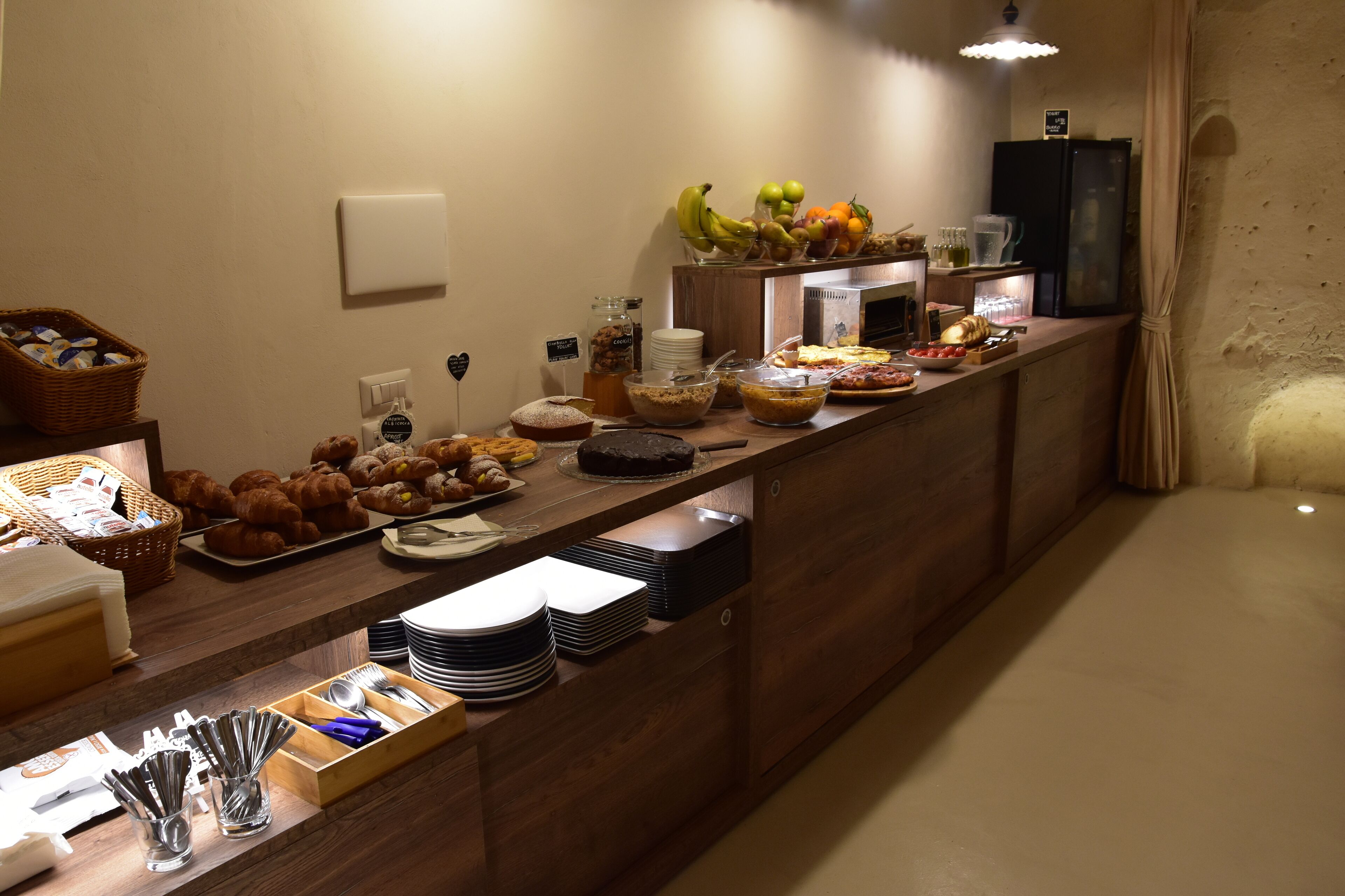 A buffet with various food items, including fruits, pastries, and a refrigerator.