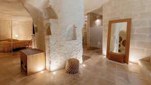 A room with a stone wall, a bed, a wooden bench, and a mirror on the wall. - Il Belvedere (Matera)