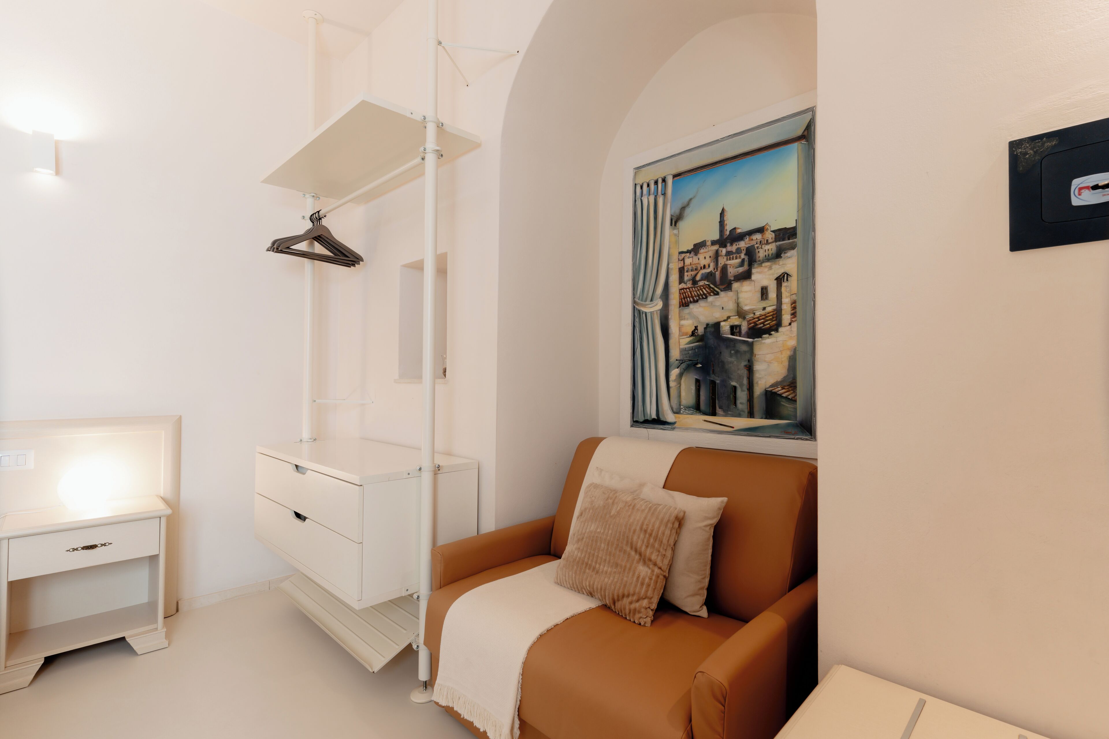 A modern room with a white desk, a brown sofa, a hanging lamp, and a painting of a cityscape.