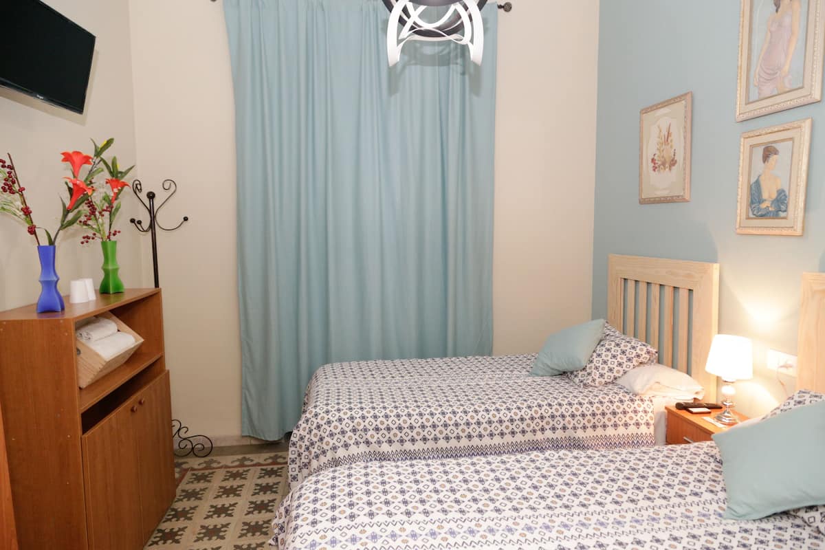 A bedroom with two beds, a wooden dresser, a TV mounted on the wall, and a window with curtains.