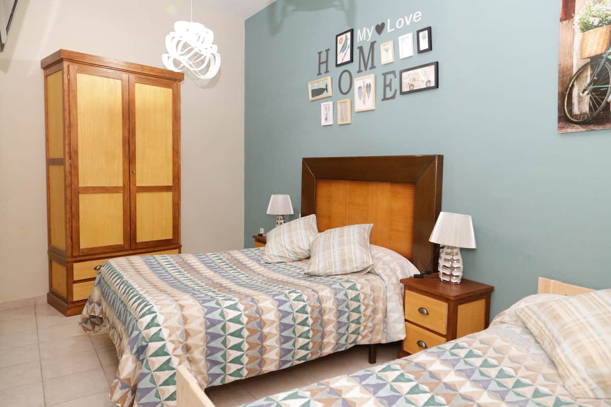A bedroom with a bed, two bedside tables, a wardrobe, and a wall with framed pictures.
