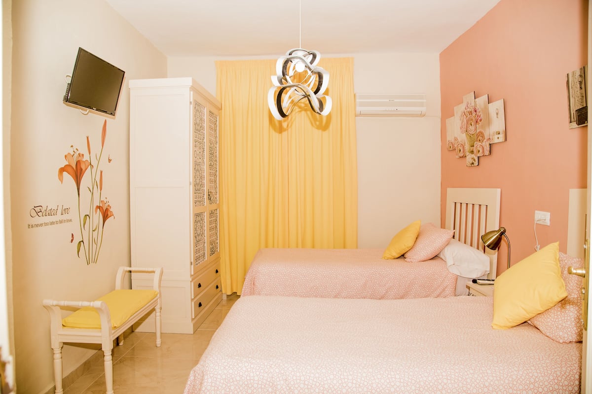 A bedroom with two beds, a desk, a chair, a TV, and a decorative wall piece.