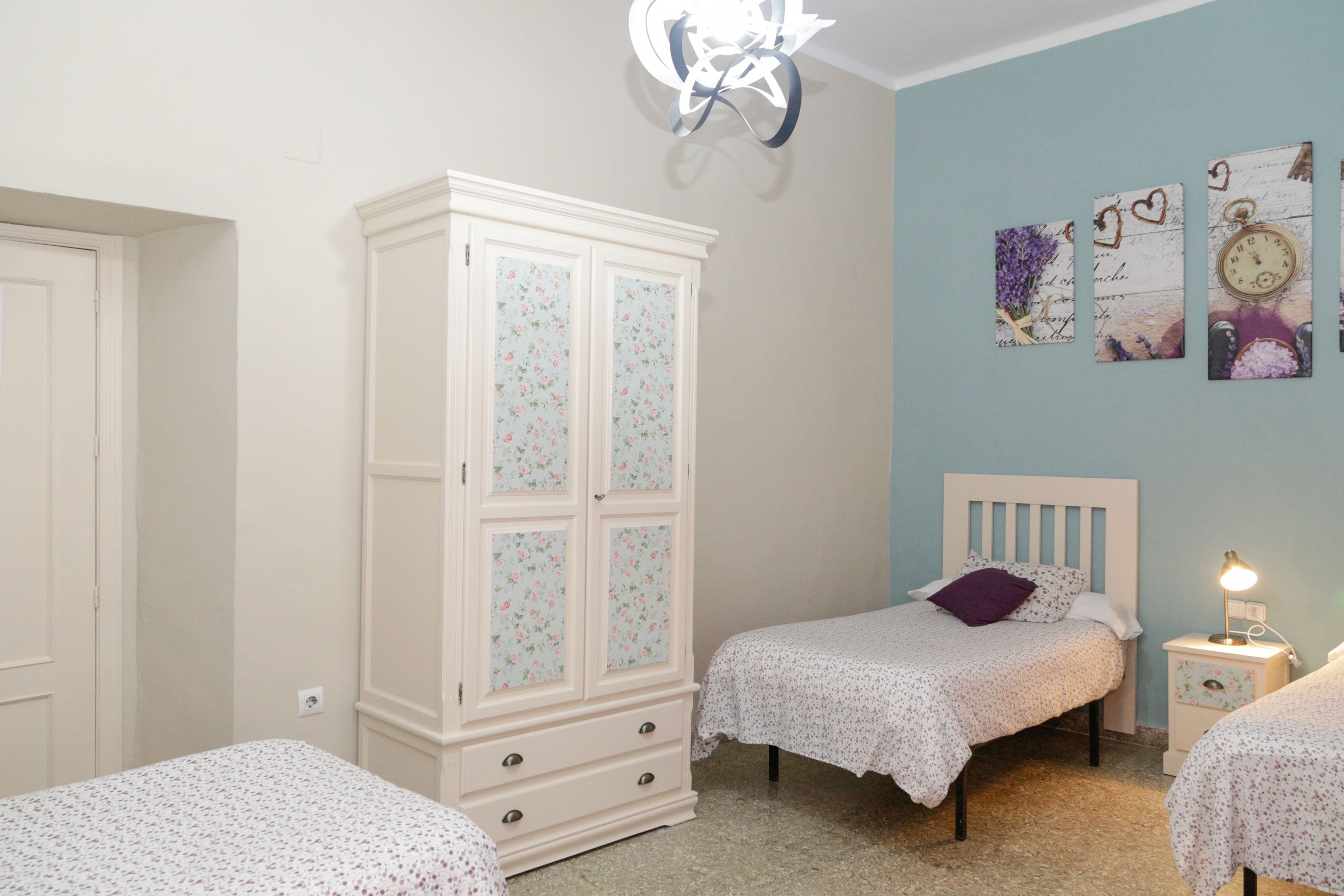 Un dormitorio con dos camas individuales, un armario blanco y una pared decorada.
