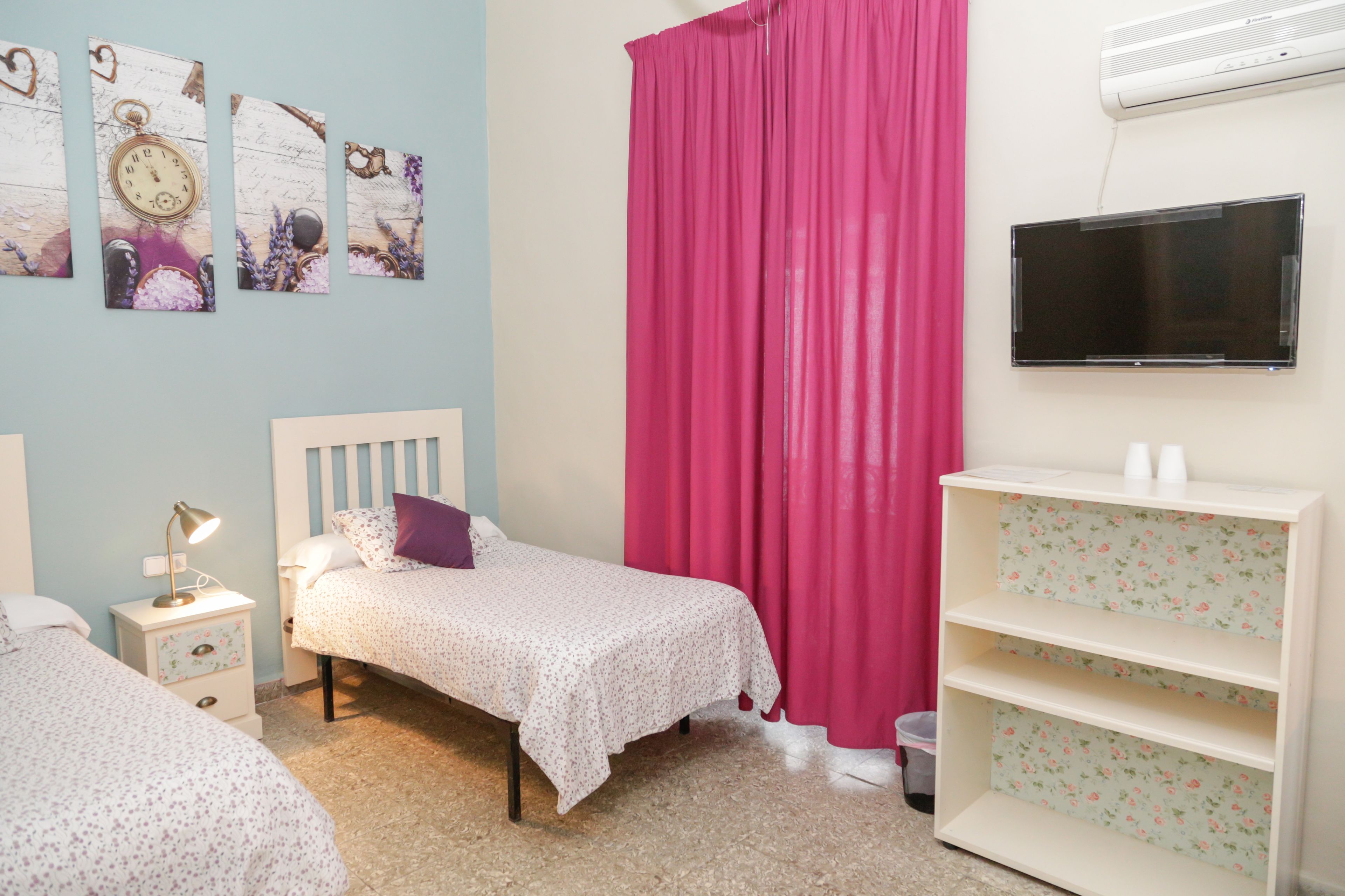 A bedroom with a bed, a nightstand, a TV, and a shelf.